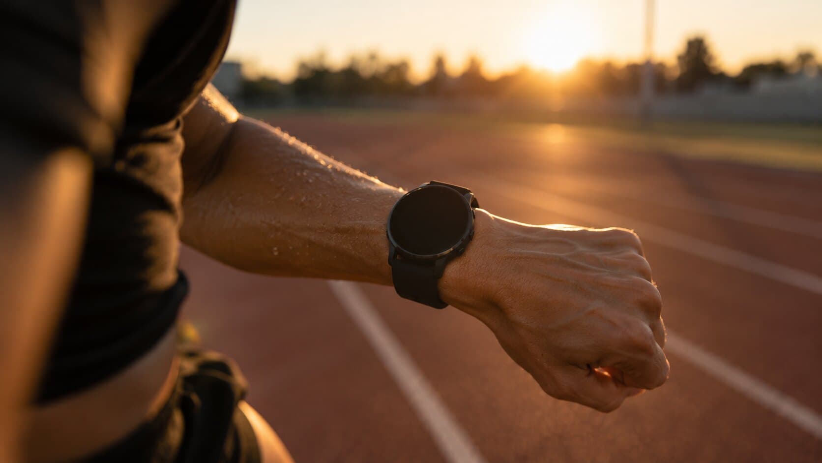 La muñeca de un corredor con su reloj, en plena zancada sobre la pista al atardecer